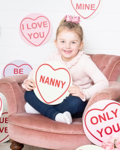 A little girl is smiling and holding a sign at a photo shoot event designed to celebrate Mother’s Day