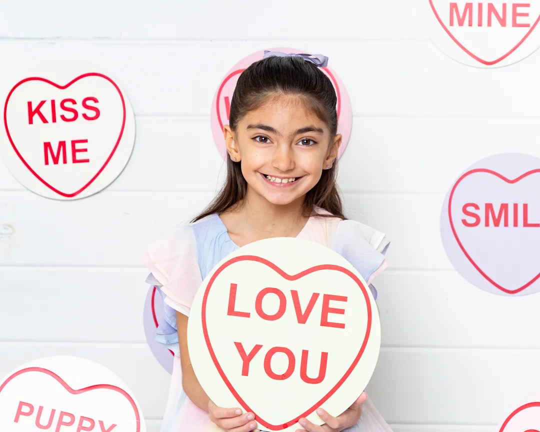 a little girl poses with a giant love heart themed candy sign that says I love you at a Mother's Day Photo Shoot
