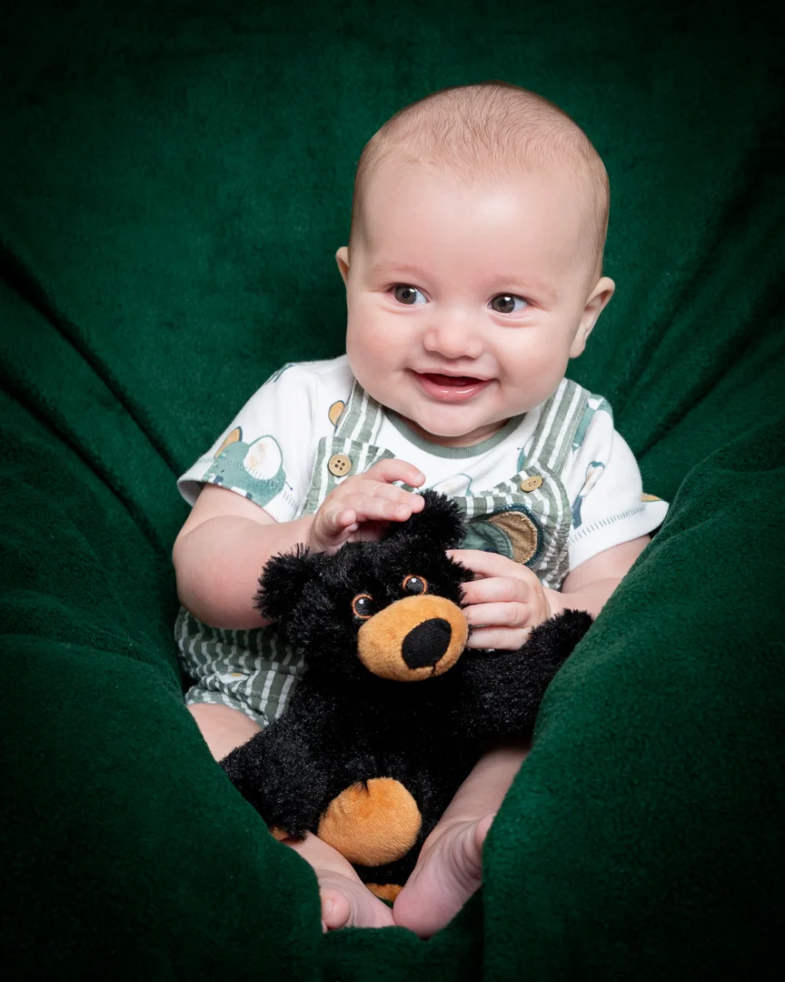 a baby and a stuffed bear toy against a green backdrop