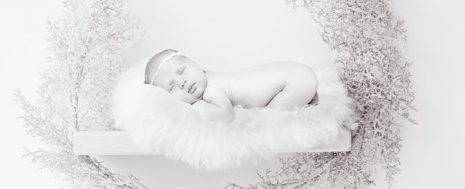 A black and white digitally composited image of a newborn sleeping on a shelf