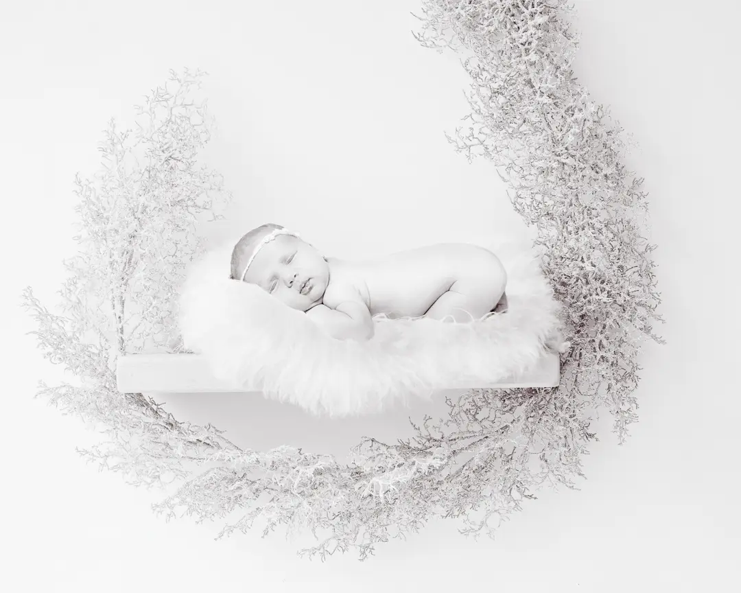 A black and white digitally composited image of a newborn sleeping on a shelf