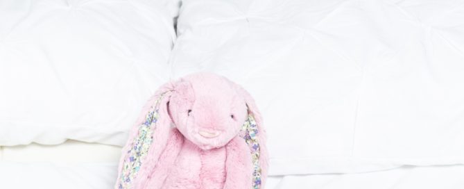 a sleeping newborn on a white bed wrapped in pink and with a pink bunny toy