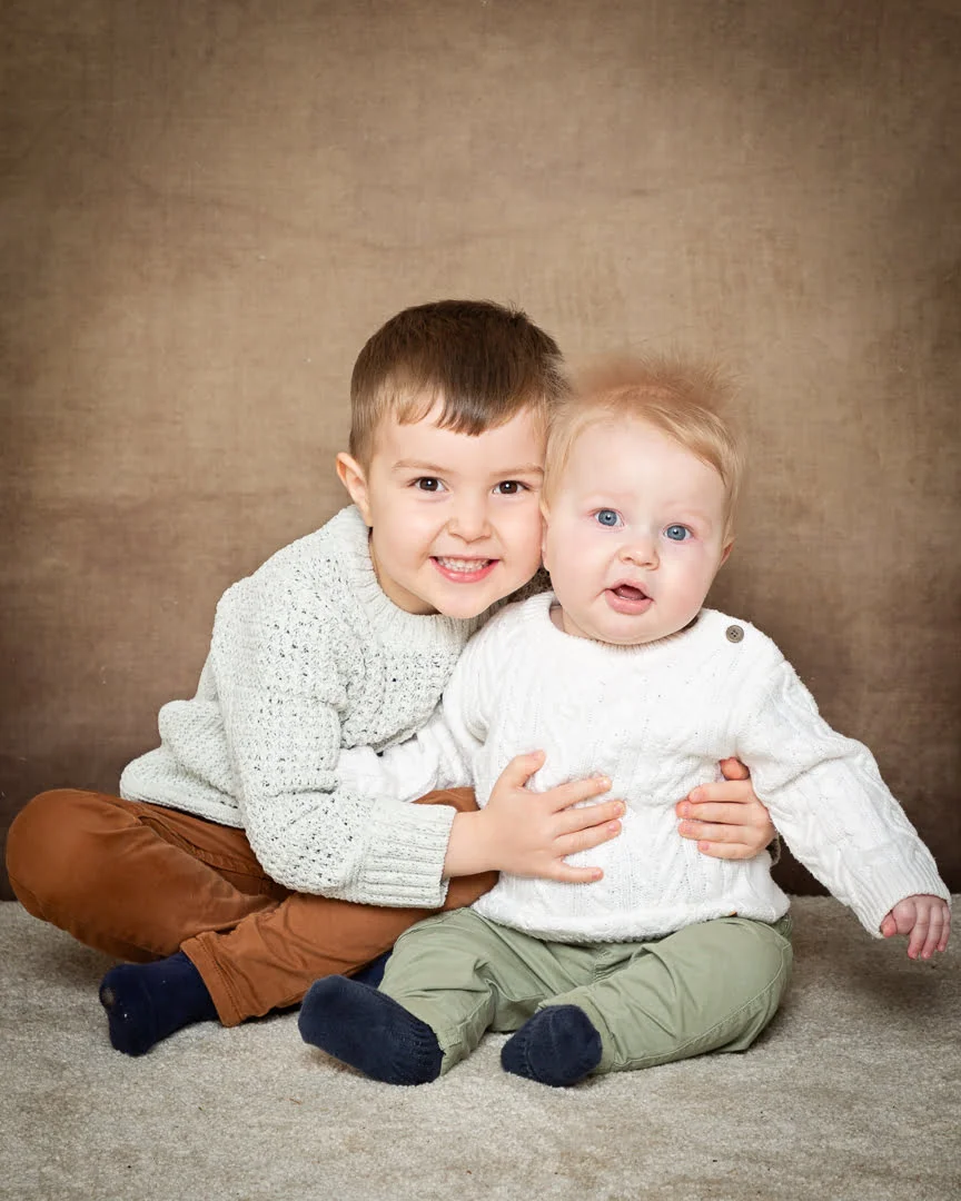 Baby Photography in East Grinstead Two brothers posing together in matching jumpers against a brown background in a studio environment