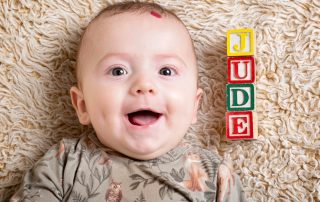 a little boy lies looking up at the camera with his name spelled out in letter blocks beside him