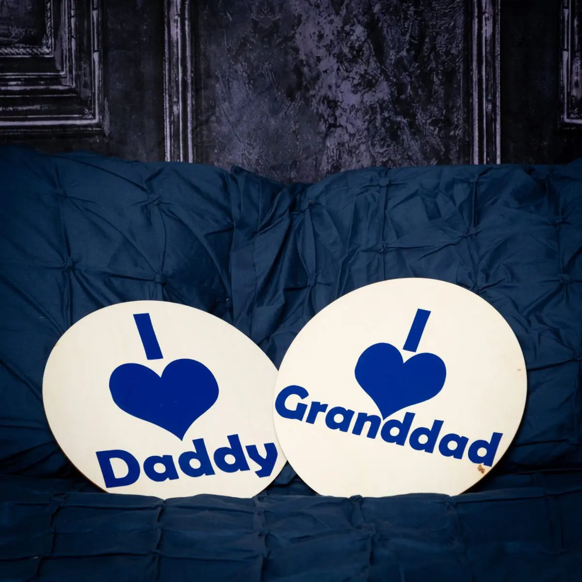 a navy bed and backdrop with two wooden signs saying I love daddy and I love Granddad