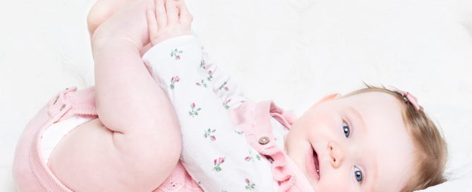 a little girl holds her toes and looks at the camera