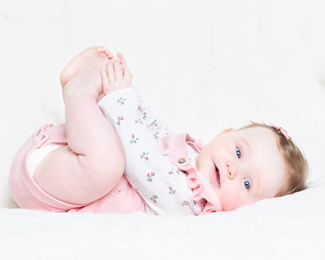 a little girl holds her toes and looks at the camera