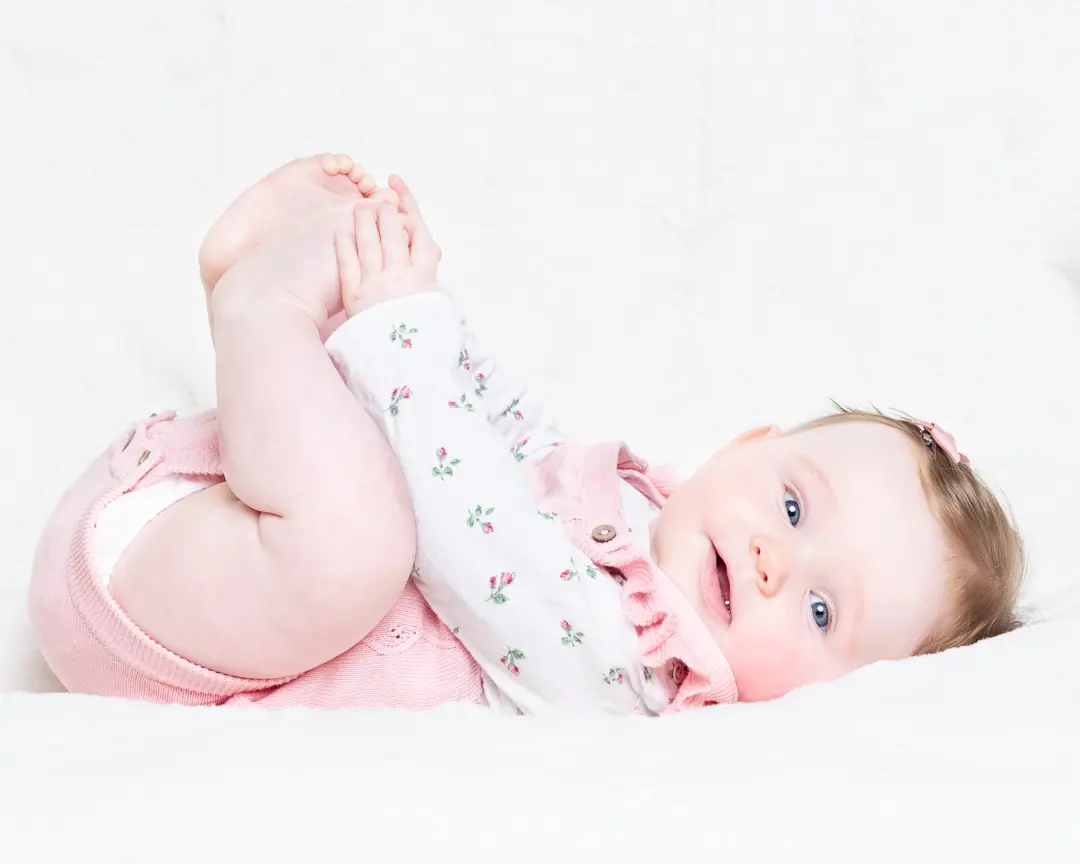 a little girl holds her toes and looks at the camera