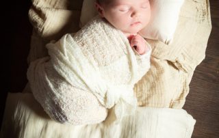 a newborn on a dark wood bed with cream bedding