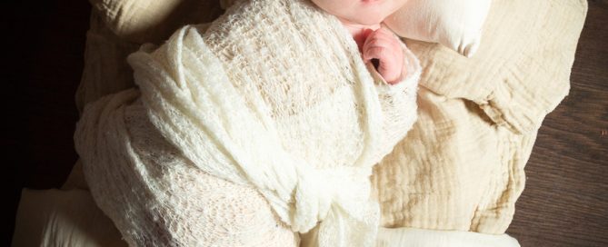 a newborn on a dark wood bed with cream bedding