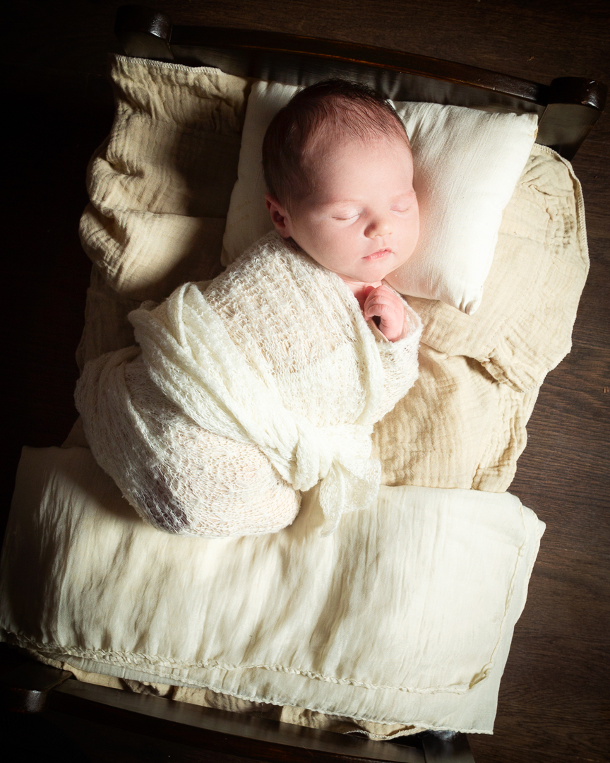 a newborn on a dark wood bed with cream bedding