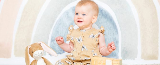 a baby with nutbrown hare props against a pastel rainbow