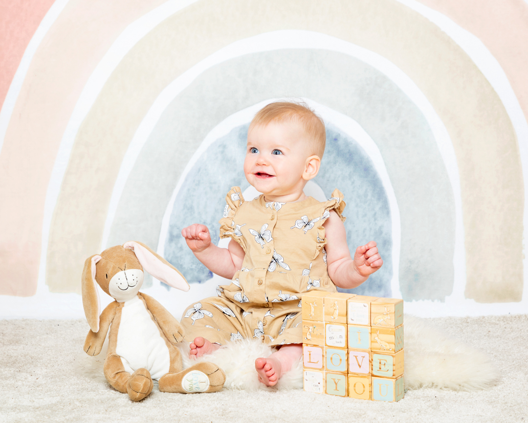 a baby with nutbrown hare props against a pastel rainbow