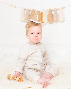 A little boy is wearing a crown with the number one on it as he looks into the camera at a professional baby photo shoot