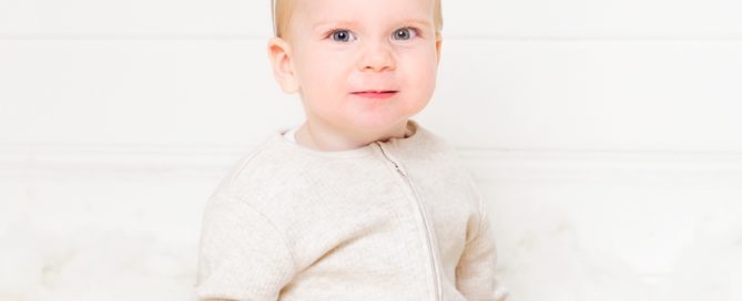 a baby in a cream romper wearing a number one crown