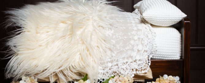 Newborn wooden bed prop with lots of cream textured bedding and flowers