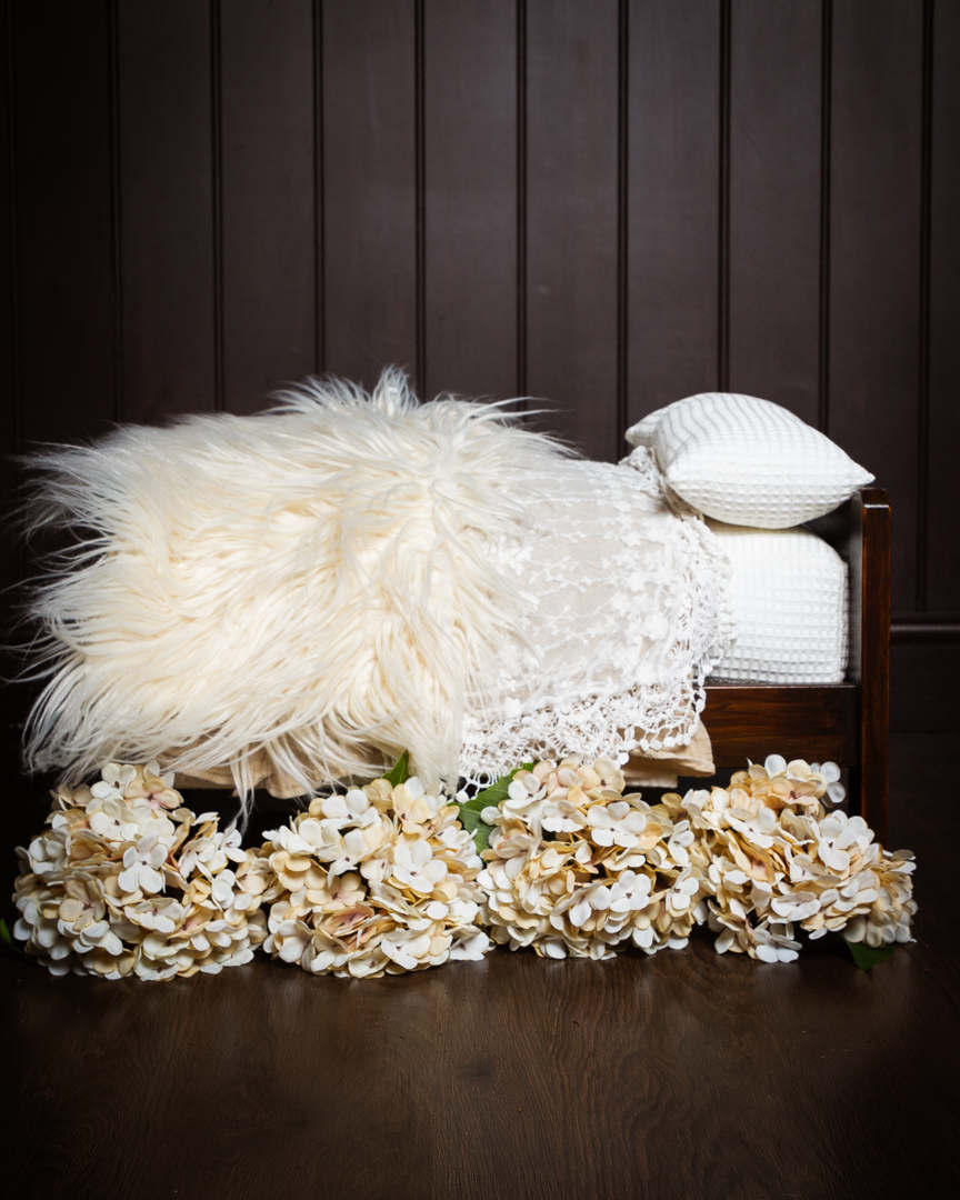 Newborn wooden bed prop with lots of cream textured bedding and flowers