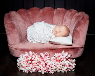 a newborn is wrapped in lace and asleep on a miniature pink chair with pink flowers