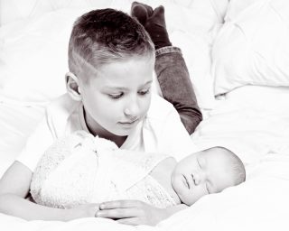 a black and white image of a big brother looking down at their newborn sibling