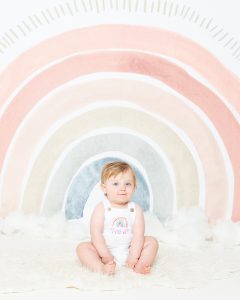 Baby Photography West Sussex a baby in a rainbow outfit against a rainbow backdrop
