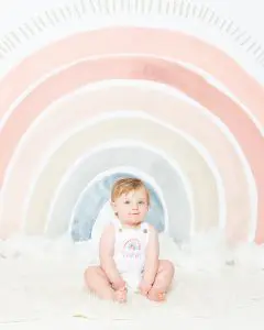 a baby in a rainbow outfit against a rainbow backdrop