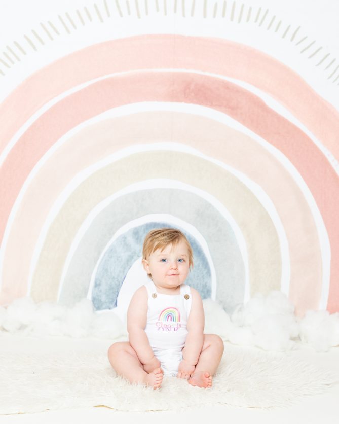 a baby in a rainbow outfit against a rainbow backdrop