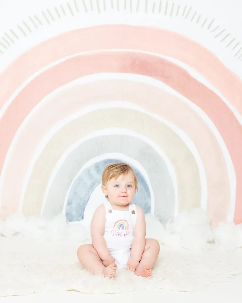 Baby Photography West Sussex a little girl in a rainbow outfit in front of a pastel rainbow backdrop