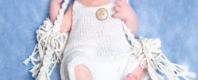 a sleeping newborn sitting on a swing and holding onto the strings