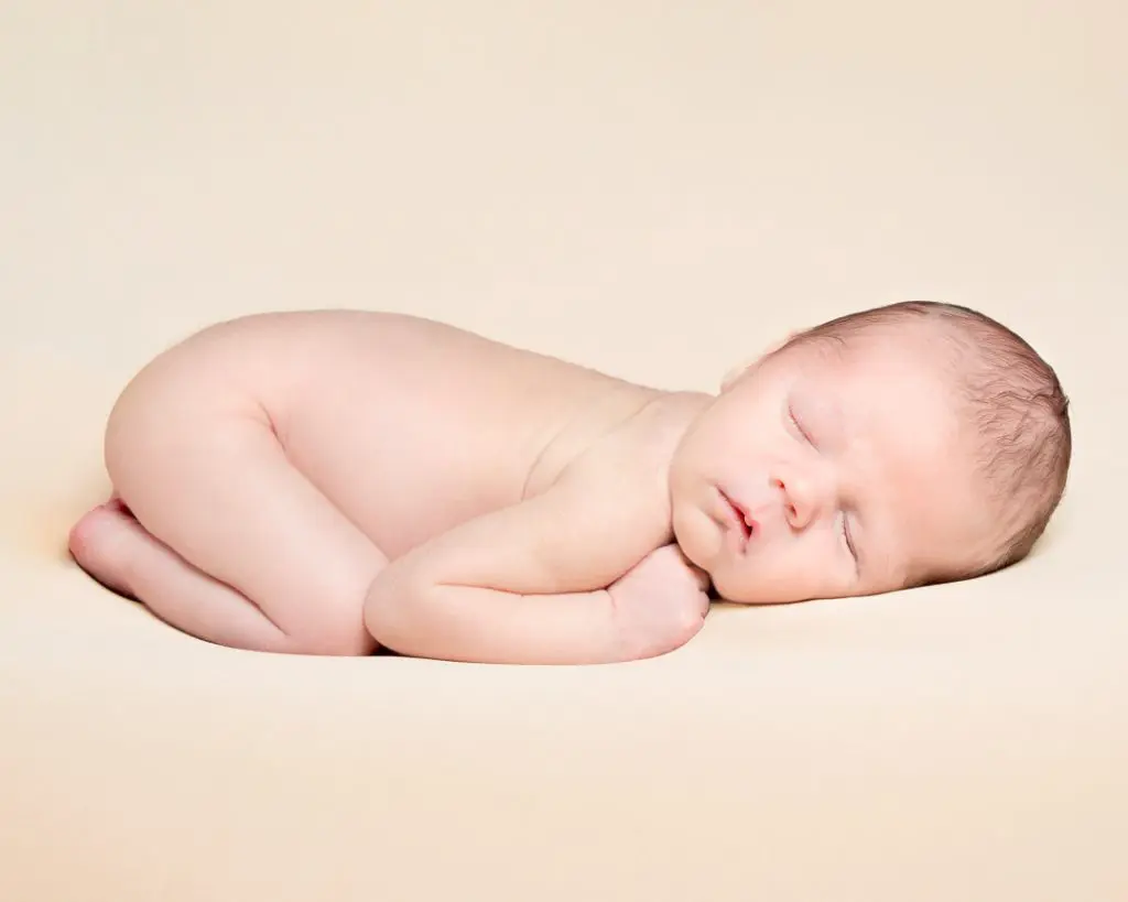 a peaceful sleeping newborn on a cream blanket