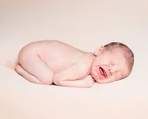 a not so peaceful sleeping newborn on a cream blanket