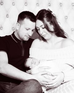 a black and white image of parents sitting on a bed holding their new baby