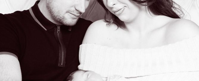 a black and white image of parents sitting on a bed holding their new baby