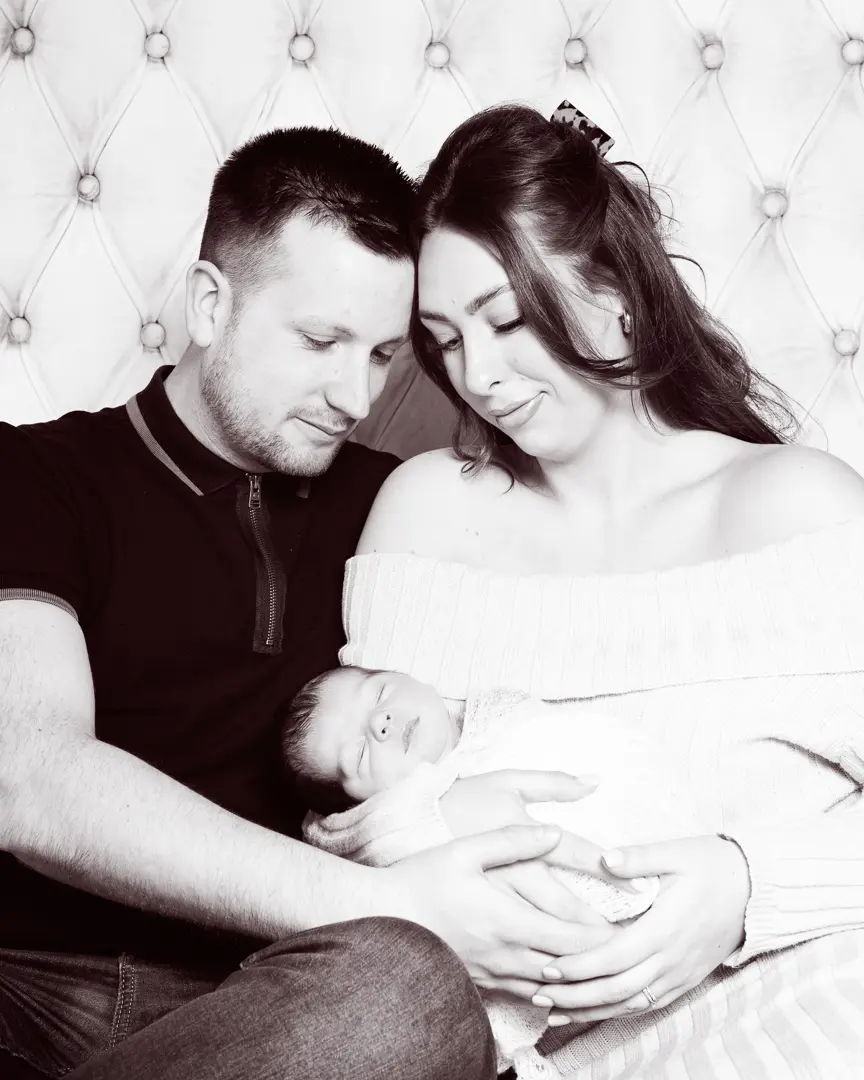 a black and white image of parents sitting on a bed holding their new baby