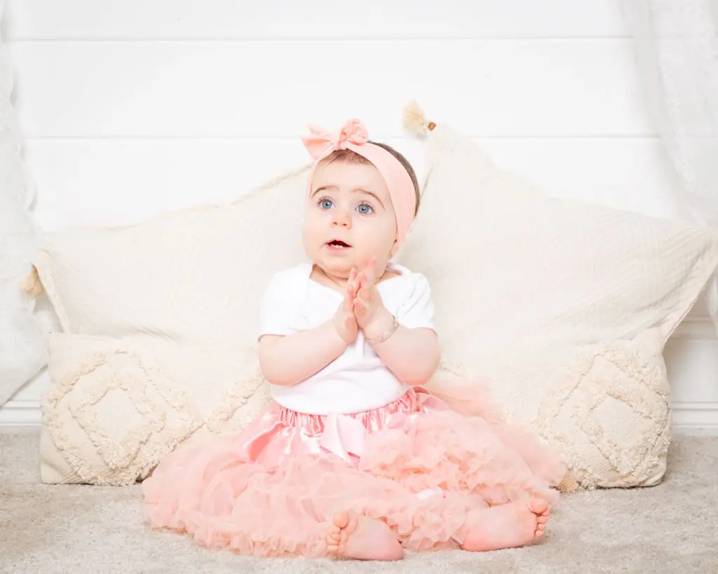 a little girl claps her hand at a photo shoot wearing a peach pettiskirt