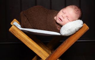 a newborn wrapped in brown and sleeping on a wooden hammock