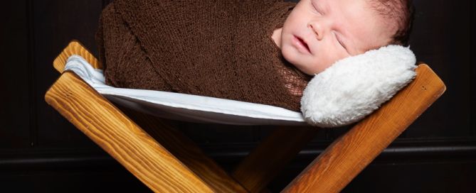 a newborn wrapped in brown and sleeping on a wooden hammock