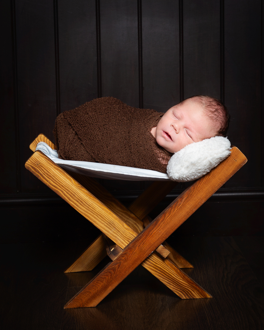 a newborn wrapped in brown and sleeping on a wooden hammock