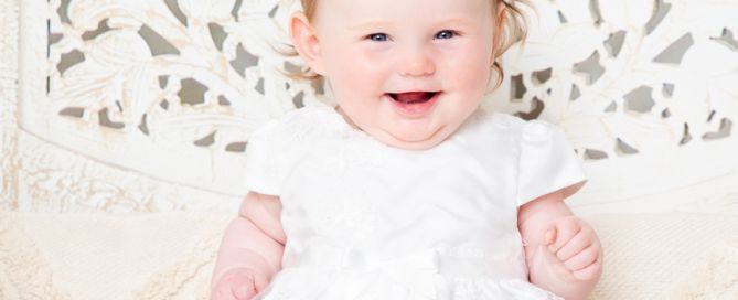 a baby in a white dress against a boho screen