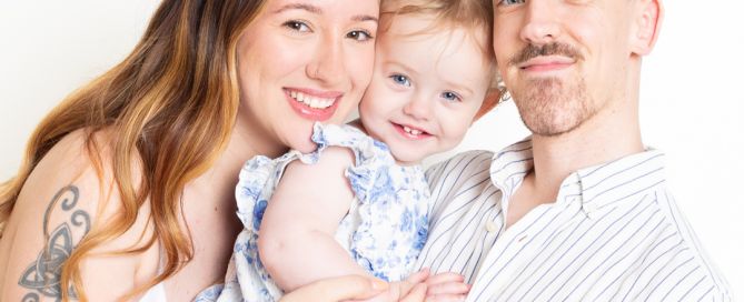 a mum and dad pose cheek to cheek with their young daughter