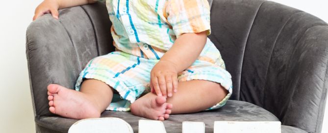 a little boy sits in a grey chair with the letters ONE sitting on the floor beneath him