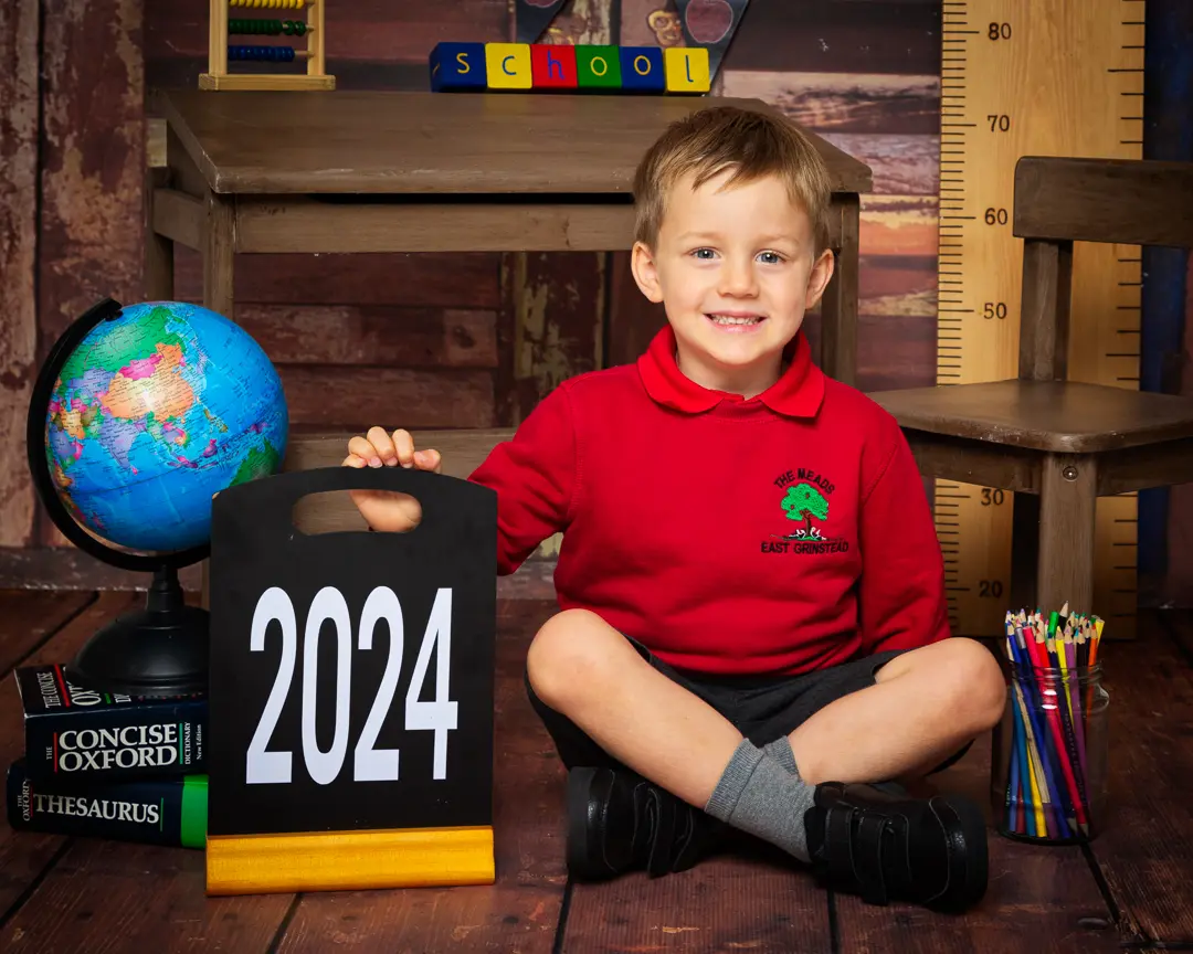 a little boy sits in a red school uniform at a starting school photo shoot
