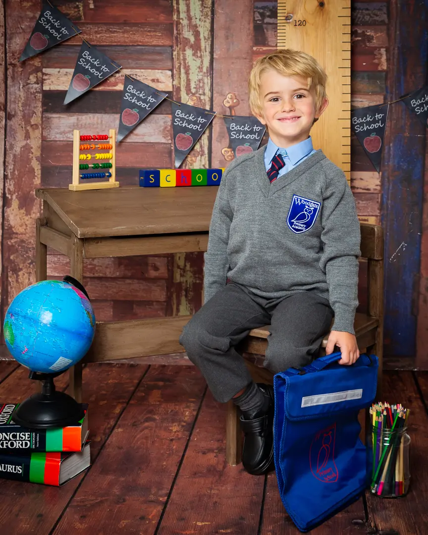 a little boy poses in a school themed set looking proud in his new grey uniform