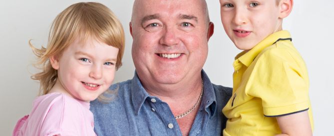 a dad holds his son and daughter on either side of him for a portrait photo