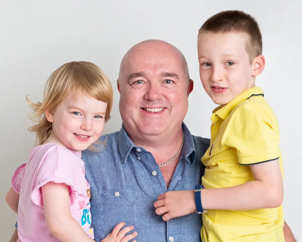 a dad holds his son and daughter on either side of him for a portrait photo