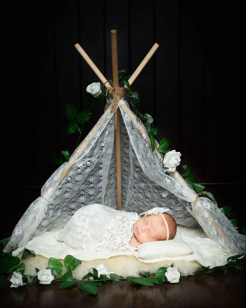 Newborn Photography in East Grinstead a newborn swaddled in white sleeping in a white miniature lace tent with white roses around her