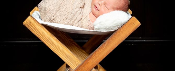 A newborn sleeping on a little wooden hammock at a photo shoot