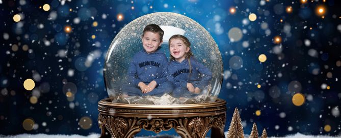 two children laugh while sitting inside a snow globe in a christmas themed digital image