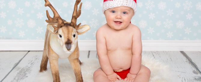 a little wears a santa outfit and sits next to a toy reindeer