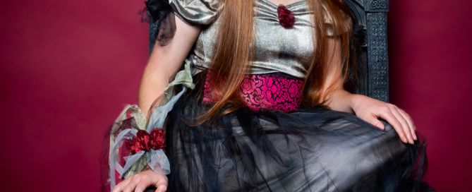 A girl in a gothic styled dress sitting on a skull throne at a Halloween photo shoot