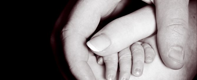 A black and white image of newborn and parents holding hands